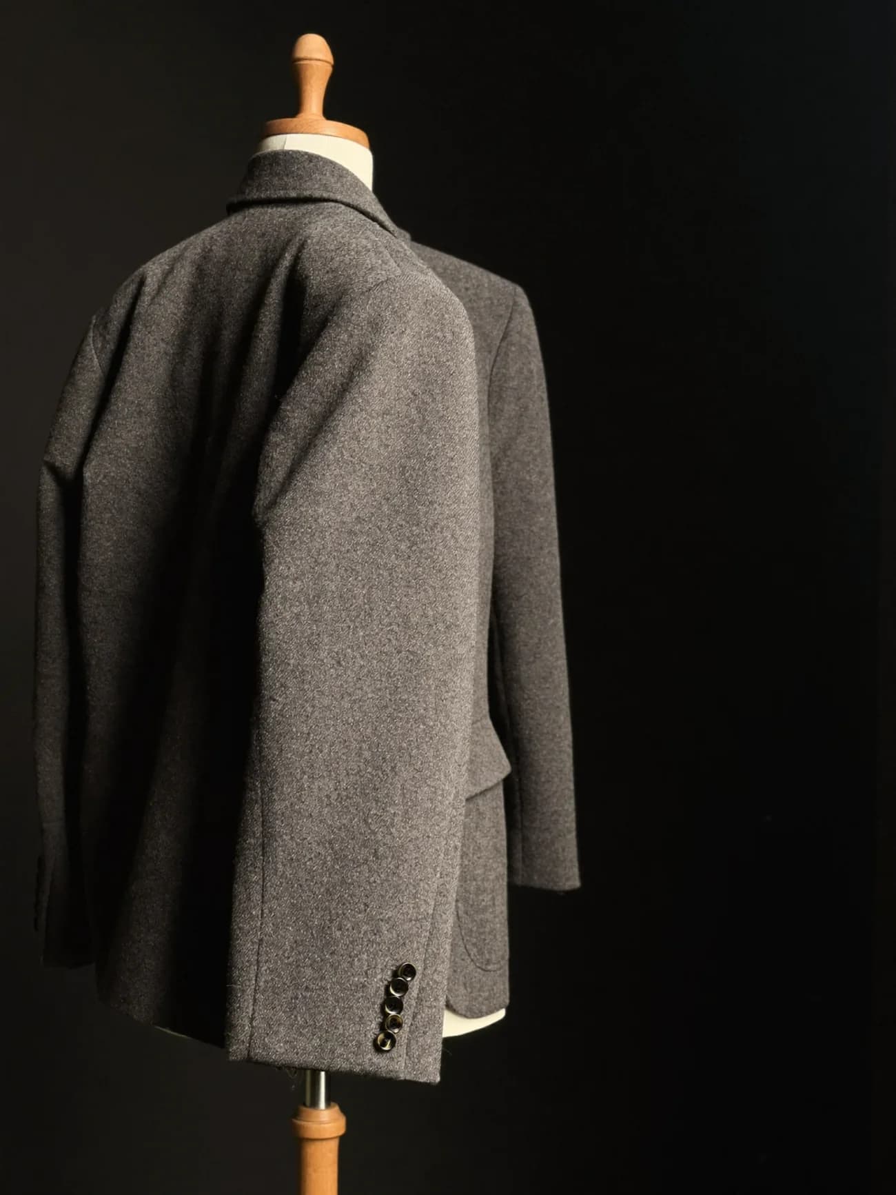 A charcoal wool jacket taking shape on a wooden tailor's mannequin