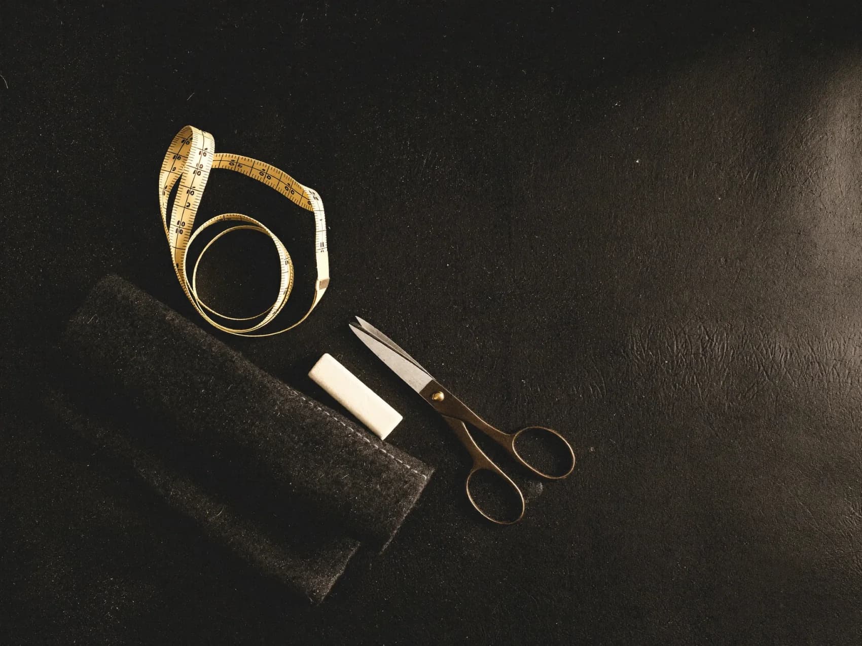 Tailor's chalk, shears, and folded charcoal cloth on a dark leather table