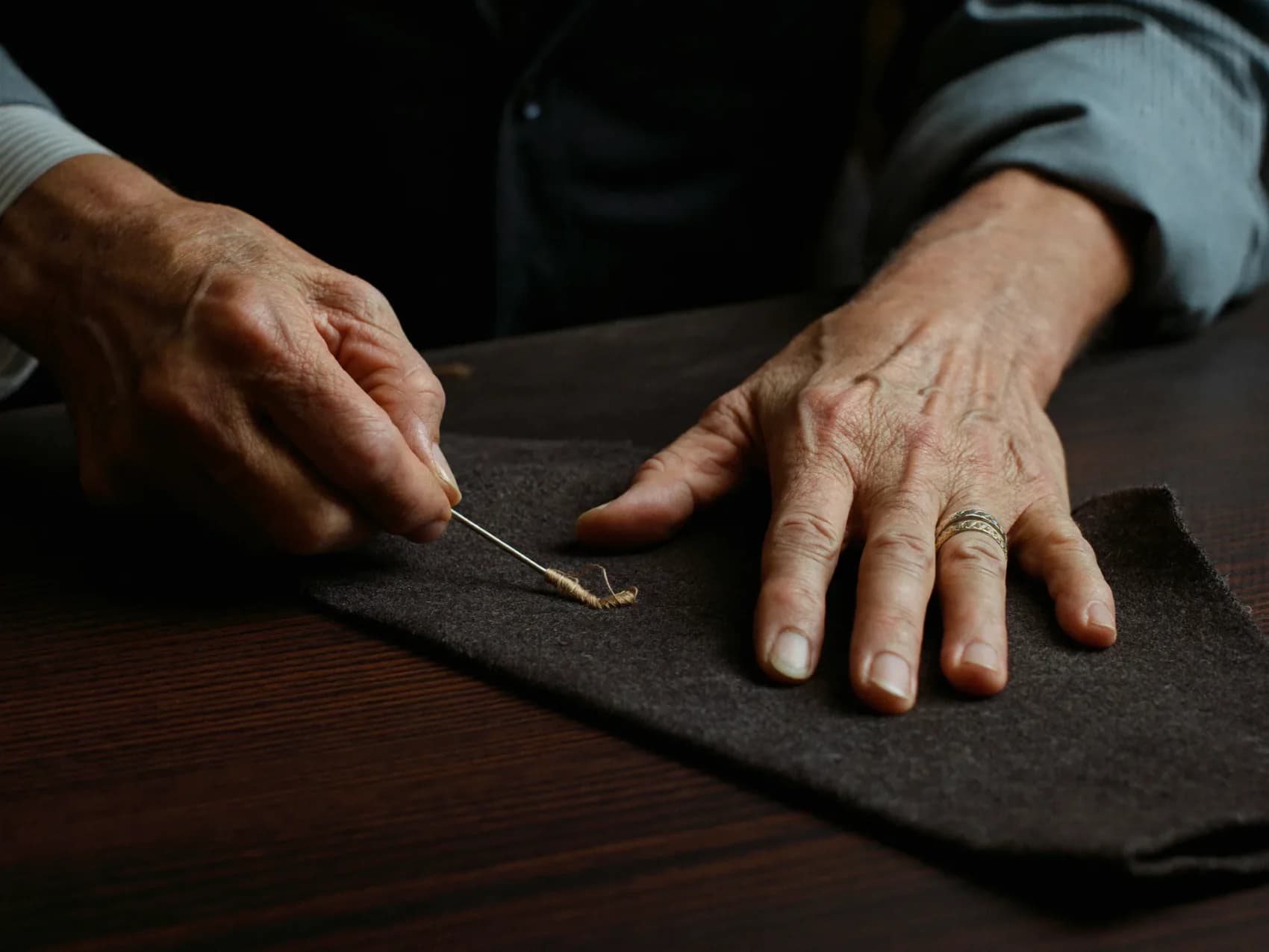 A master tailor's hands drawing waxed thread through a charcoal lapel