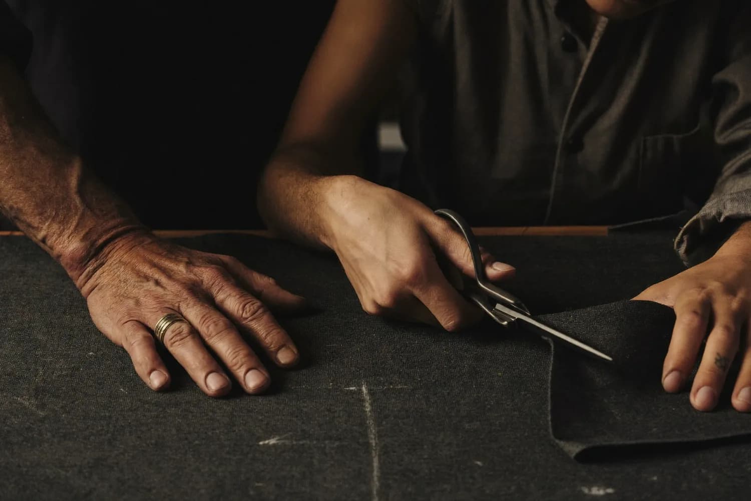 Master tailor guiding an apprentice's hands at the bench